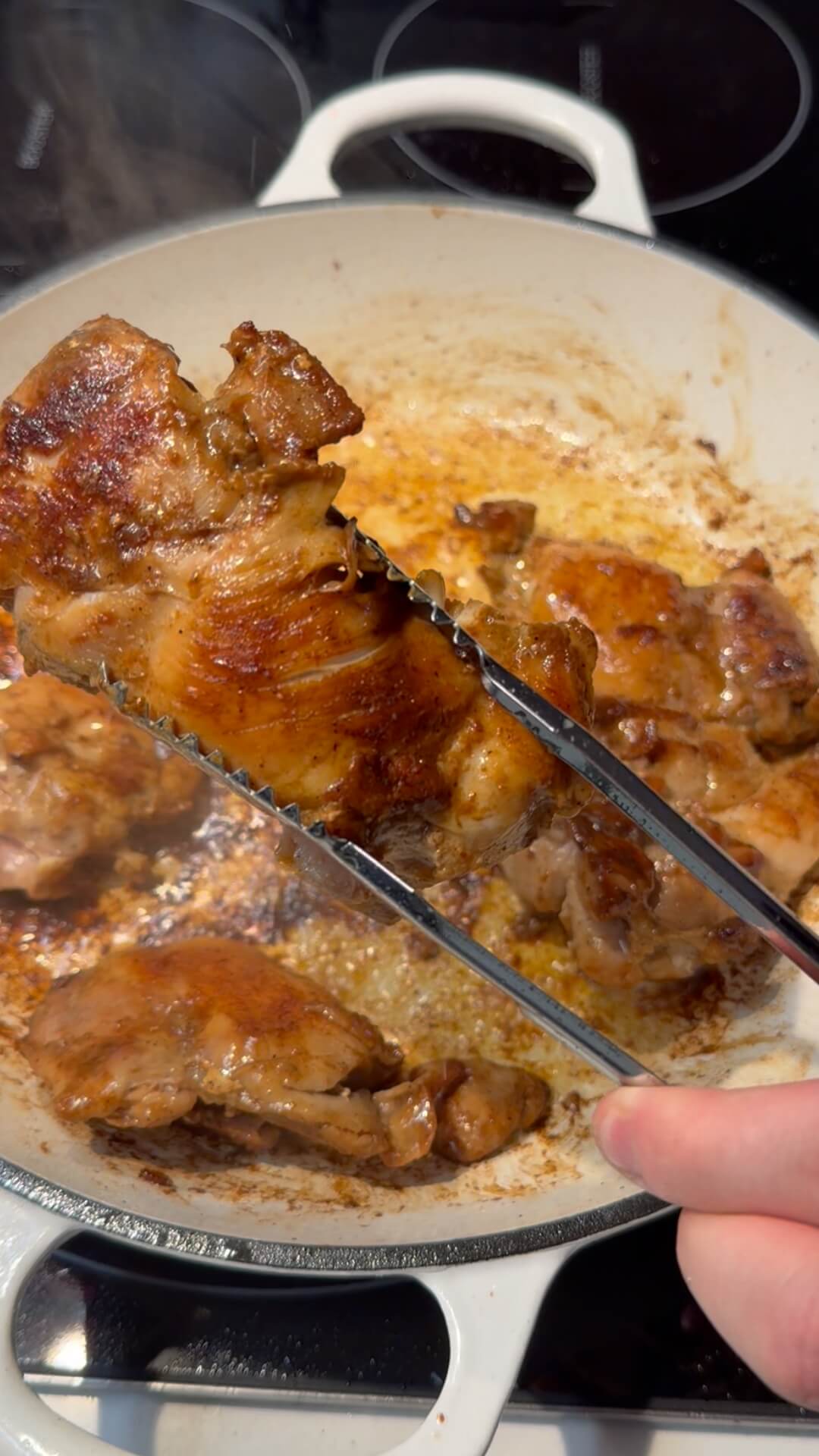 Seared golden-brown chicken thighs being cooked in a white enameled pan.