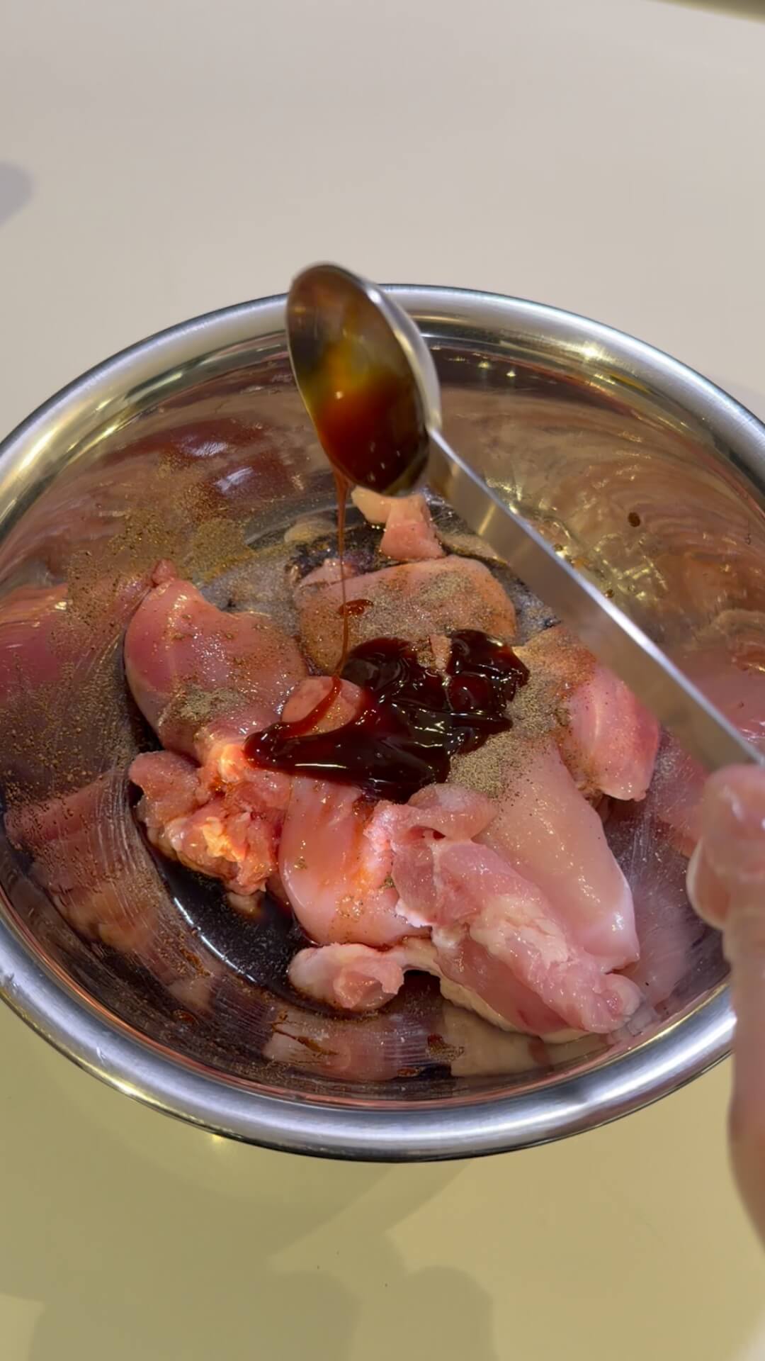 Raw chicken thighs in a silver mixing bowl with soy sauce and oyster sauce before being mixed.