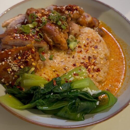 A bowl of Thai Red Curry Chicken with seared chicken thighs, jasmine rice, and bok choy.