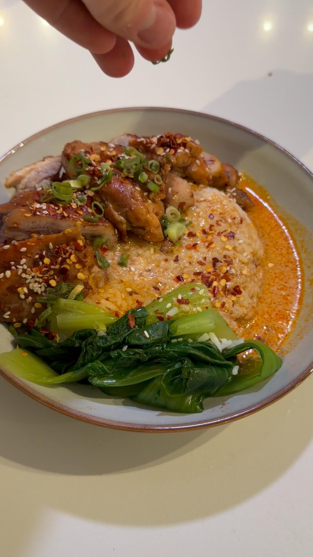 A bowl of Thai Red Curry Chicken with seared chicken thighs, jasmine rice, and bok choy.