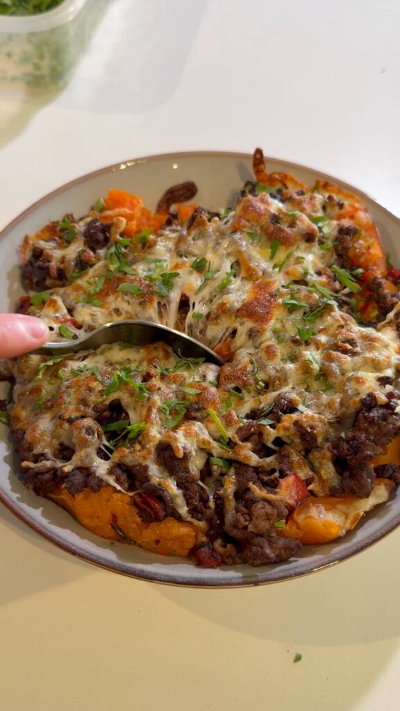 A close-up, top-down view of a loaded sweet potato bowl being garnished with fresh herbs by hand.