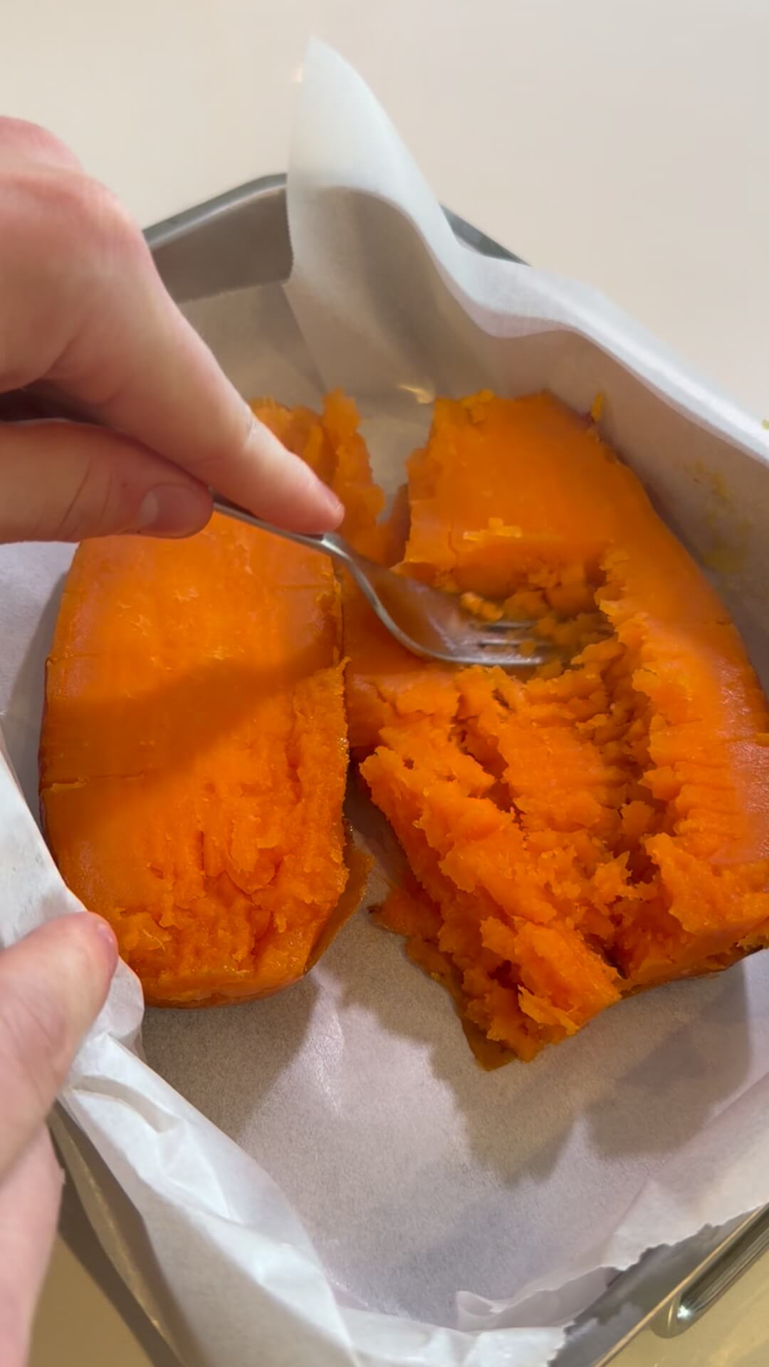 Cooked beef mince being layered onto a bed of mashed orange sweet potato in a baking dish lined with parchment paper.Layering the savory beef filling onto the mashed sweet potato base.