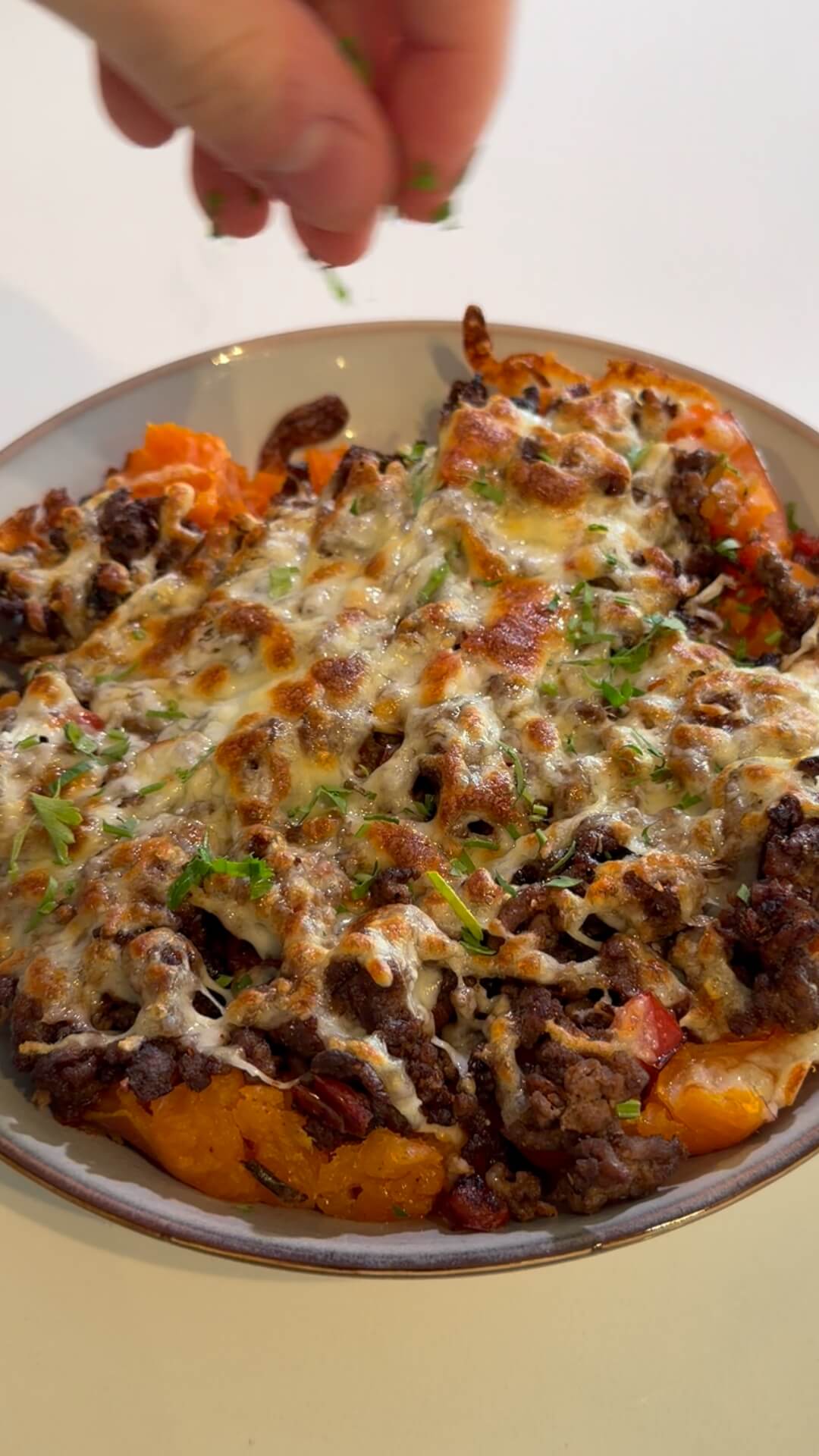 A top-down close-up of a loaded sweet potato burrito bowl, featuring mashed orange sweet potato topped with seasoned beef mince, melted golden-brown mozzarella cheese, and fresh green garnish.
