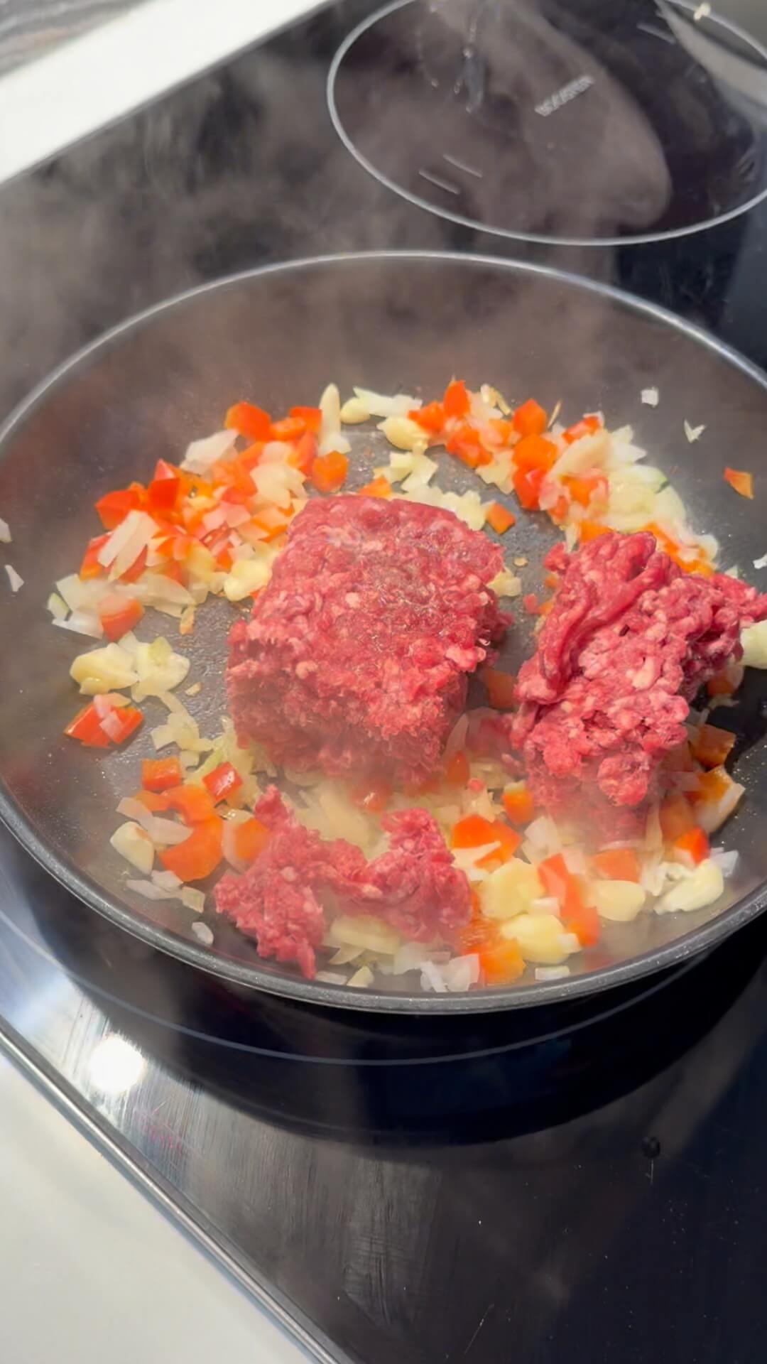 Raw beef mince placed in the center of a frying pan, surrounded by sautéed diced onion and red capsicum.
